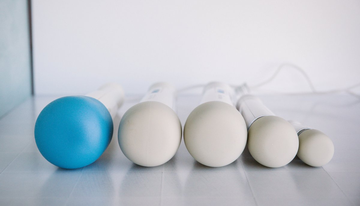 The Vibratex Magic Wands. The Magic Wand Original is on the far left, with a blue silicone cap covering its vinyl head. To its right are the Magic Wand Plus, the Magic Wand Rechargeable, Magic Wand Mini, and Magic Wand Micro.