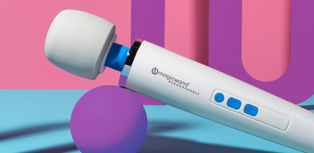 Square image of the Vibratex Magic Wand Rechargeable. The massager is tilted upwards with the handle balancing precariously on a purple ball. The pink background contrasts with the blue and white of the wand massager. Purple, contrasting, geometric shapes are in the background of the image. | Kinkly Shop