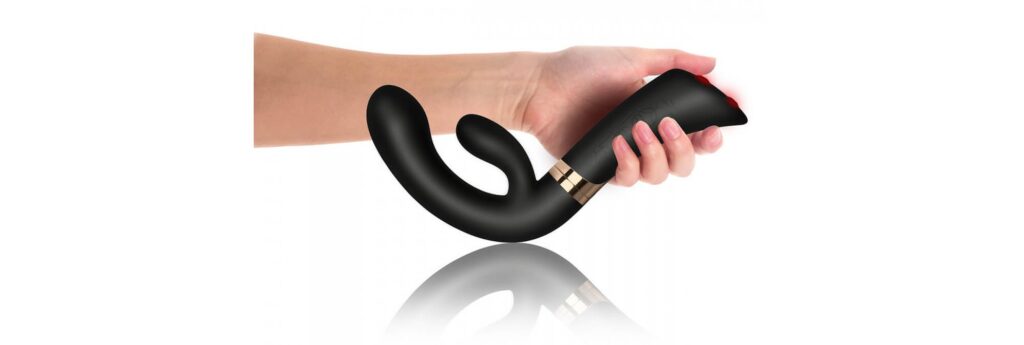 A hand holds the Rocks-Off Enigma Fuzion with the shaft facing towards the hand owner. This angle showcases the drastic curve of the insertable portion of the vibrator to make it easier to grip and use. | Kinkly Shop